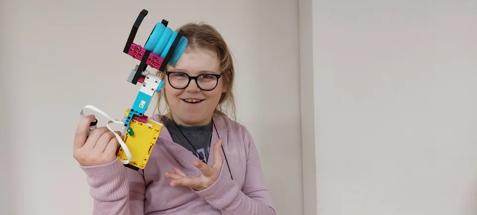 Uśmiechnięte dziecko pokazujące własną konstrukcję LEGO zbudowaną na warsztatach robotyki w Poznaniu